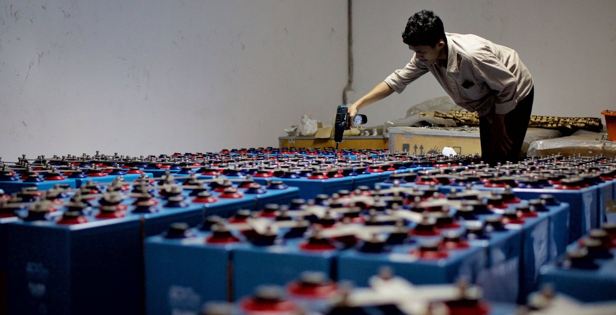 Technician working across banks of industrial batteries in a battery room