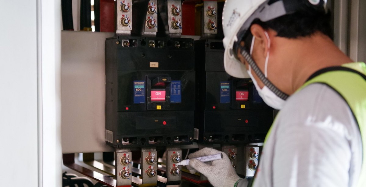 Technician marking torque witness stripes on circuit breaker terminals in a switchgear cabinet
